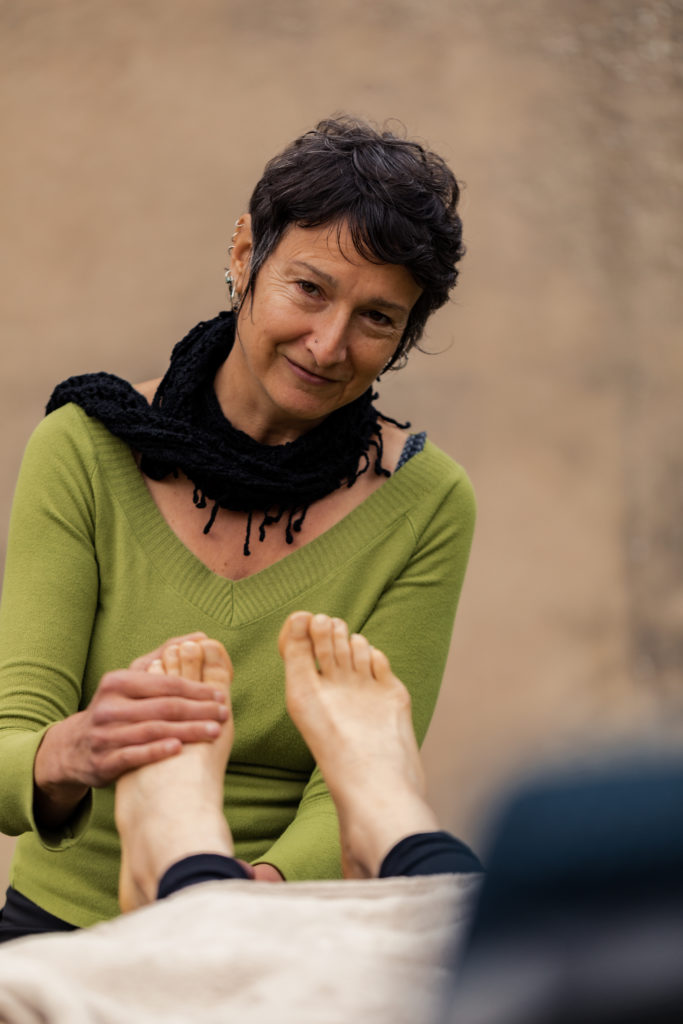C'est une photo de Sarah Hirsch qui effectue des gestes de réflexologie plantaire sur les pieds d'une personne. 